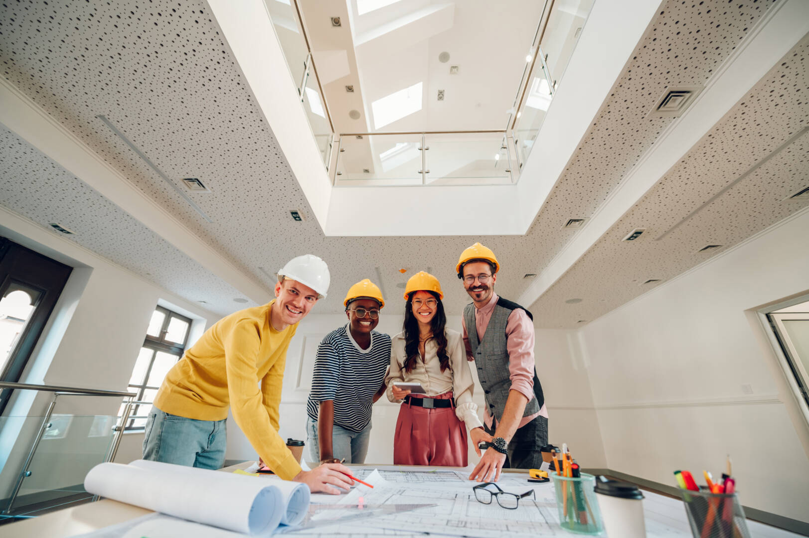 Multiracial group of architects gathering at table with papers and gadgets while sharing ideas about new project they are working on. Looking into the camera. Modern building design. Copy space.